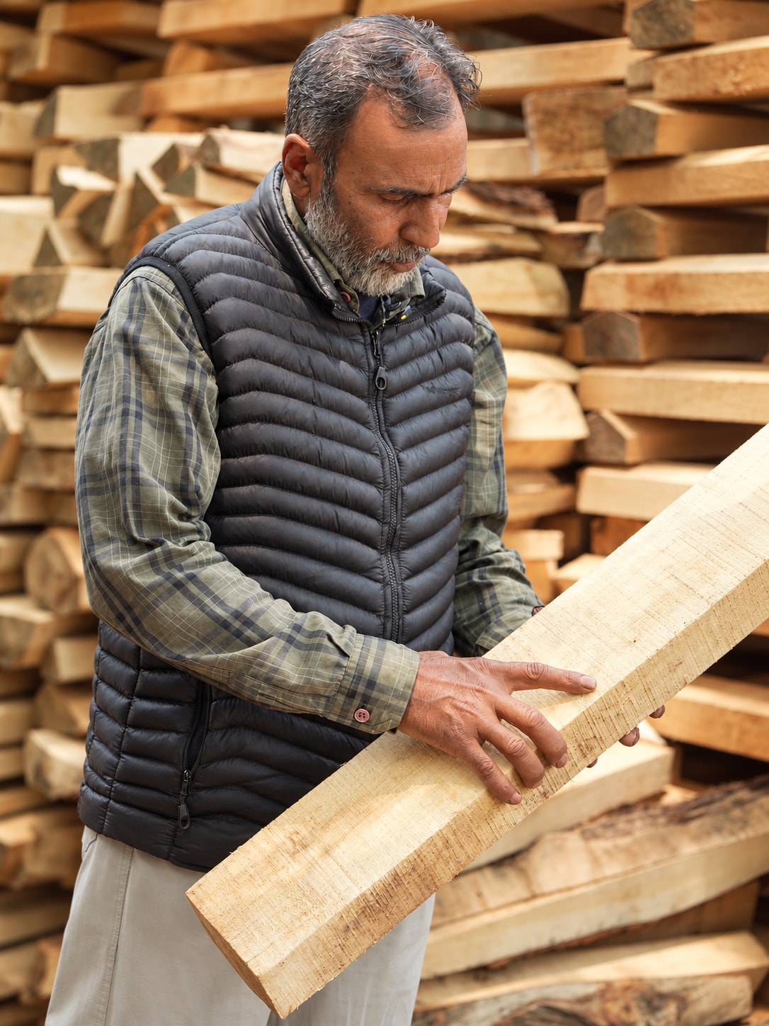 The founder’s father examines the grain of a raw willow cleft, holding it in his hands beside stacks of willow