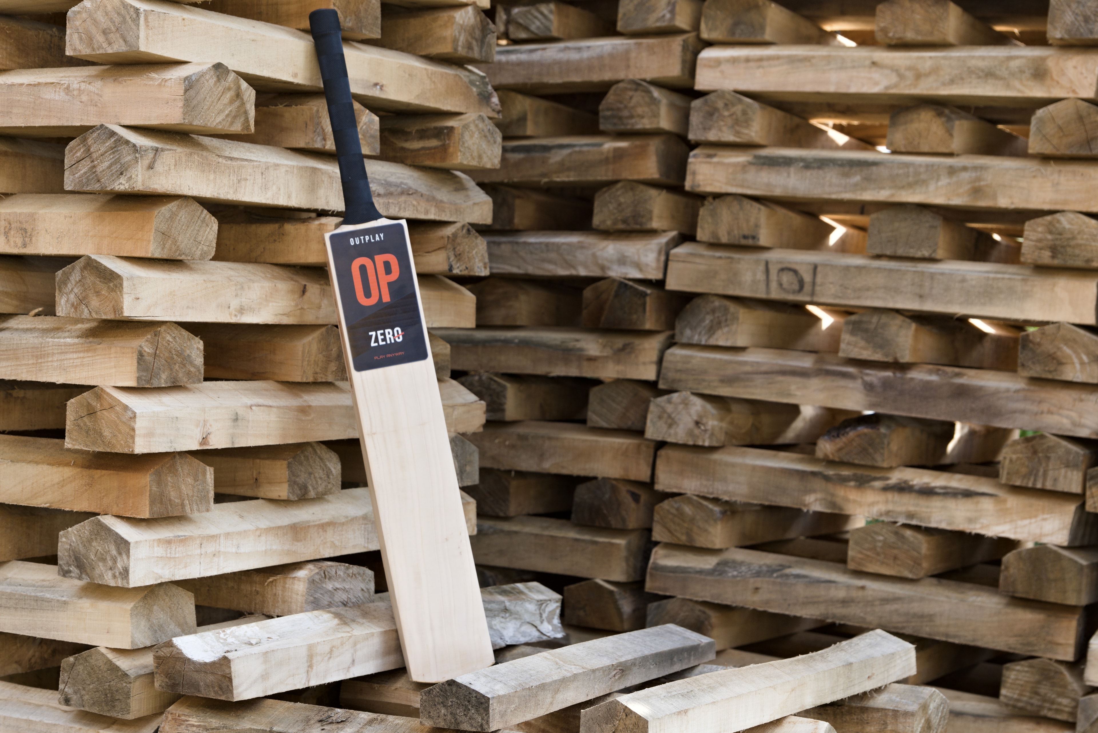 OUTPLAY ZERO resting against stacks of willow, with its full blade and black grip visible