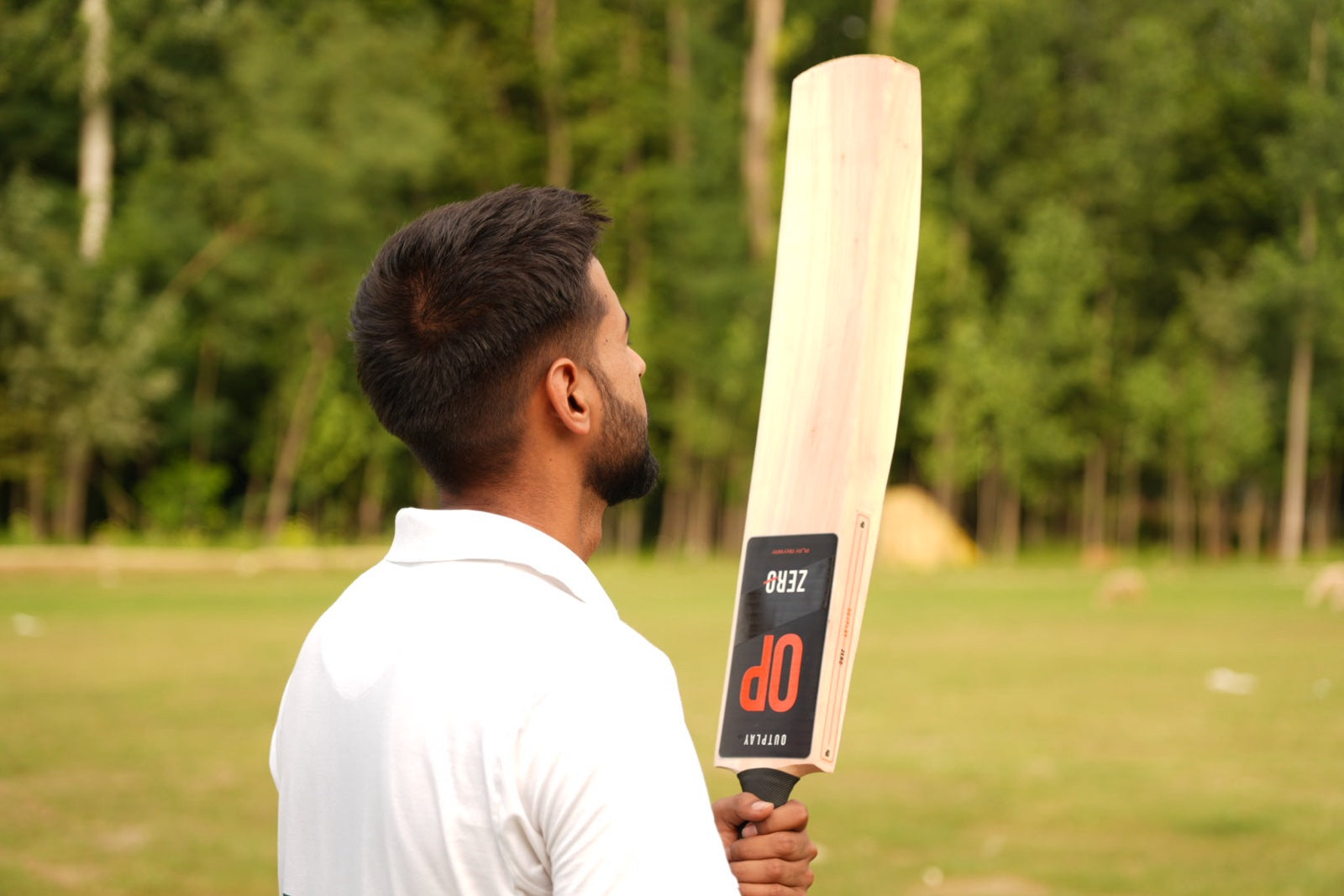 Player holding OUTPLAY ZERO on a cricket ground